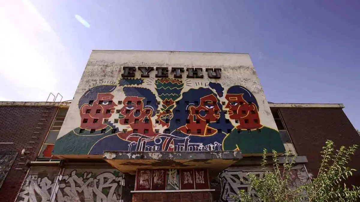 Colorful mural on a building facade with stylized faces and graffiti, under a clear blue sky.
