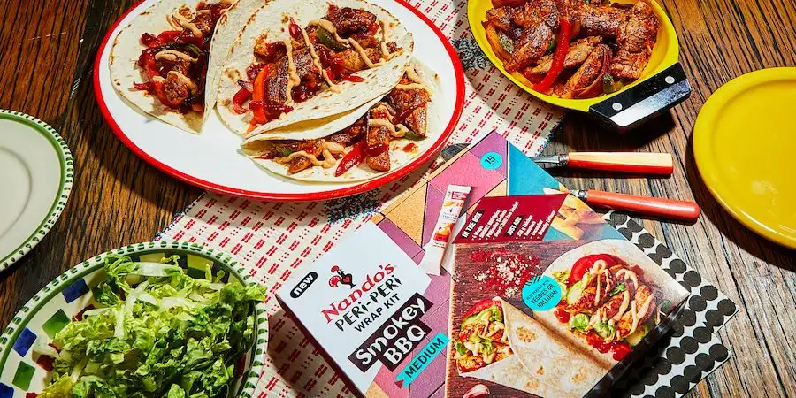 Nando's PERi-PERi wraps with grilled chicken, veggies, and salad on a table with packaging and plates.